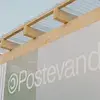 Sign reading "Postevand" on a modern structure with wooden beams and clear panels, set against a blue sky.